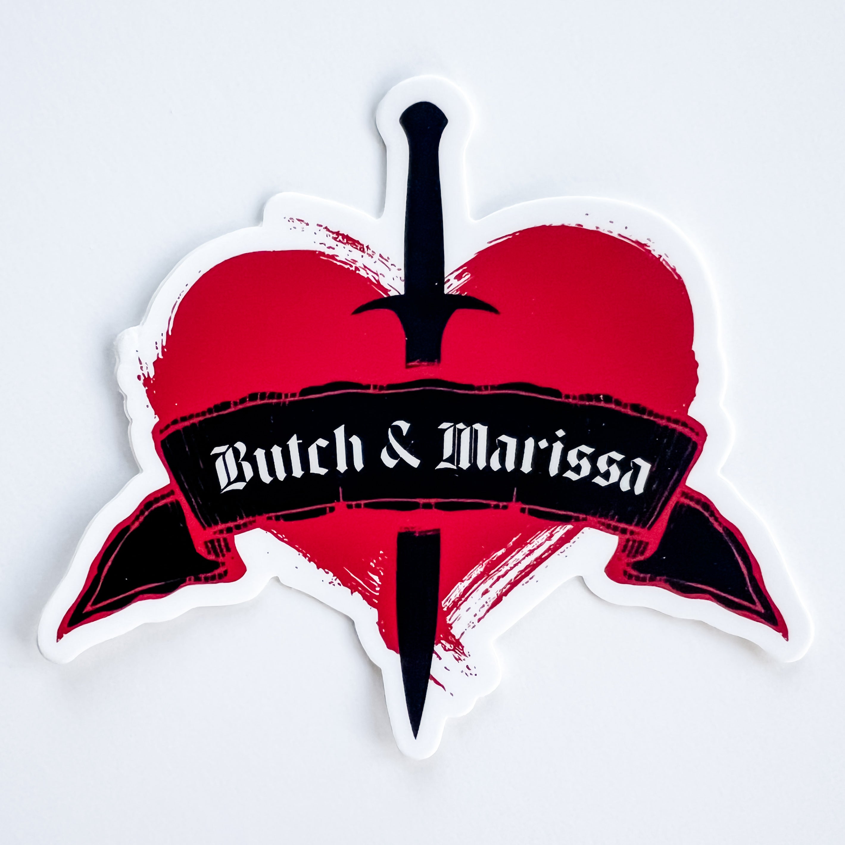 Heart-shaped sticker with a dagger and 'Butch & Marissa' text on a white background