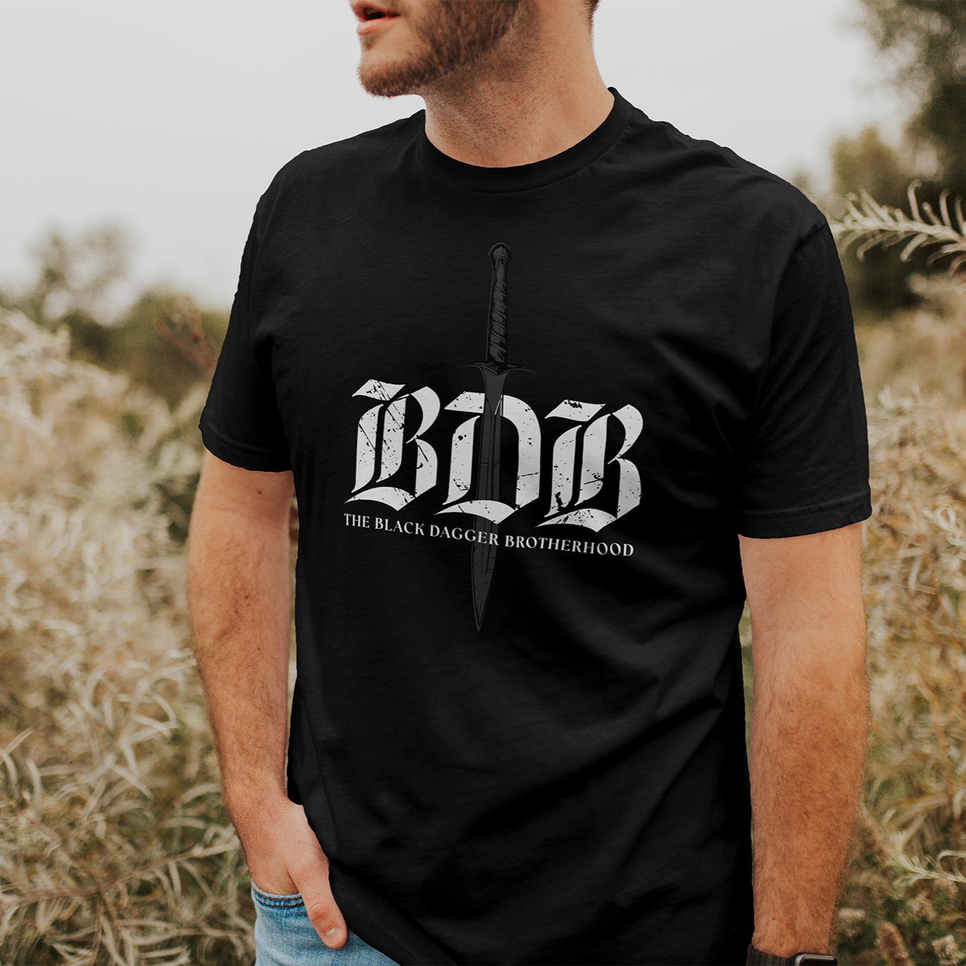 Man wearing a black t-shirt with 'BDB' logo in a field
