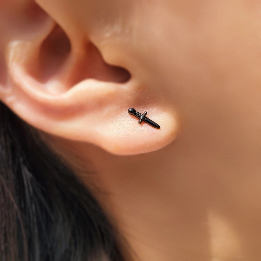 a close up image of a woman's ear wearing a small black dagger earring
