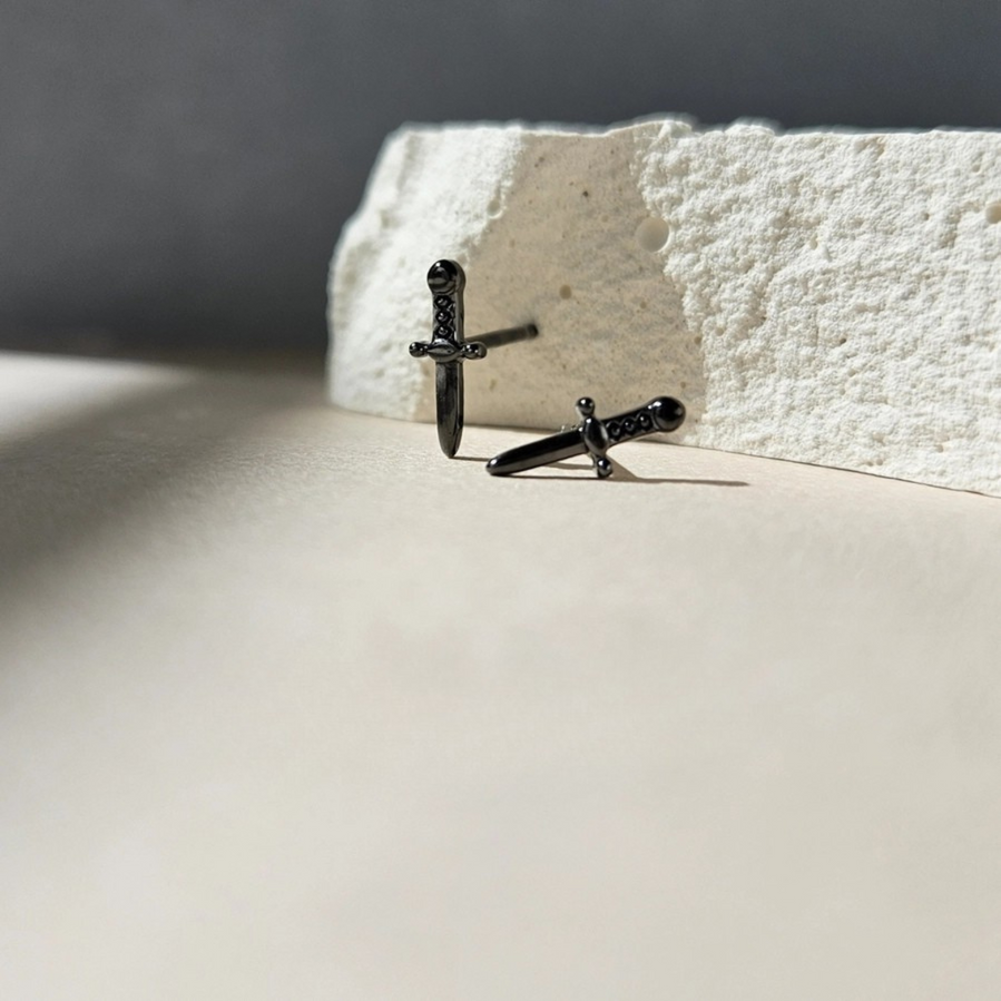 a pair of black dagger earrings are posed artfully by a rock