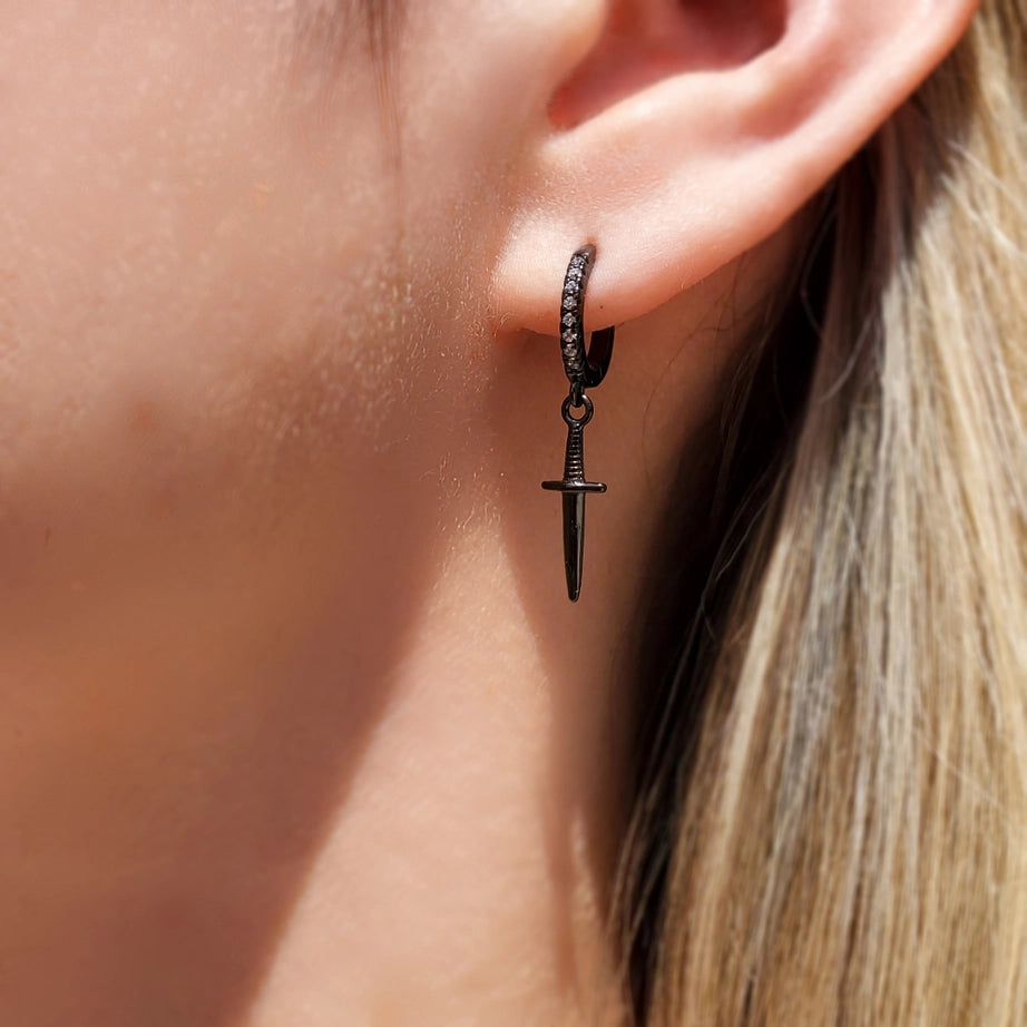 a woman wears a hoop earring encrusted with diamonds. A black dagger hangs from the hoop.