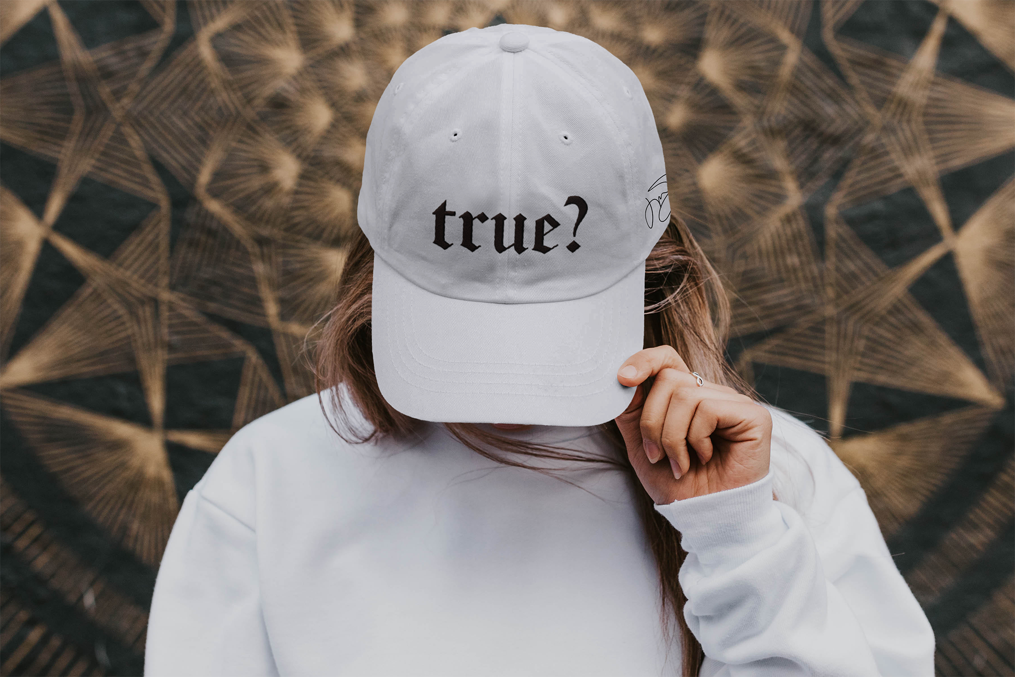 A woman wears a white ballcap with the visor tilted down. The cap reads "true?"