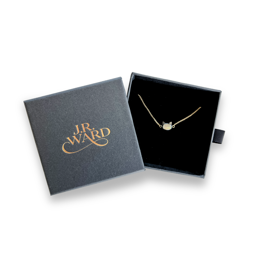 Gold bracelet with mother of pearl cat charm in a J.R. Ward jewelry box on a white background