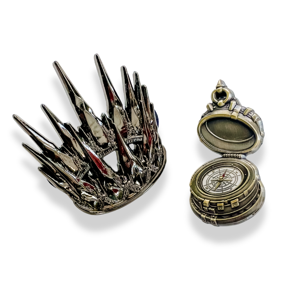 black spiked crown and open compass enamel pins on a white background