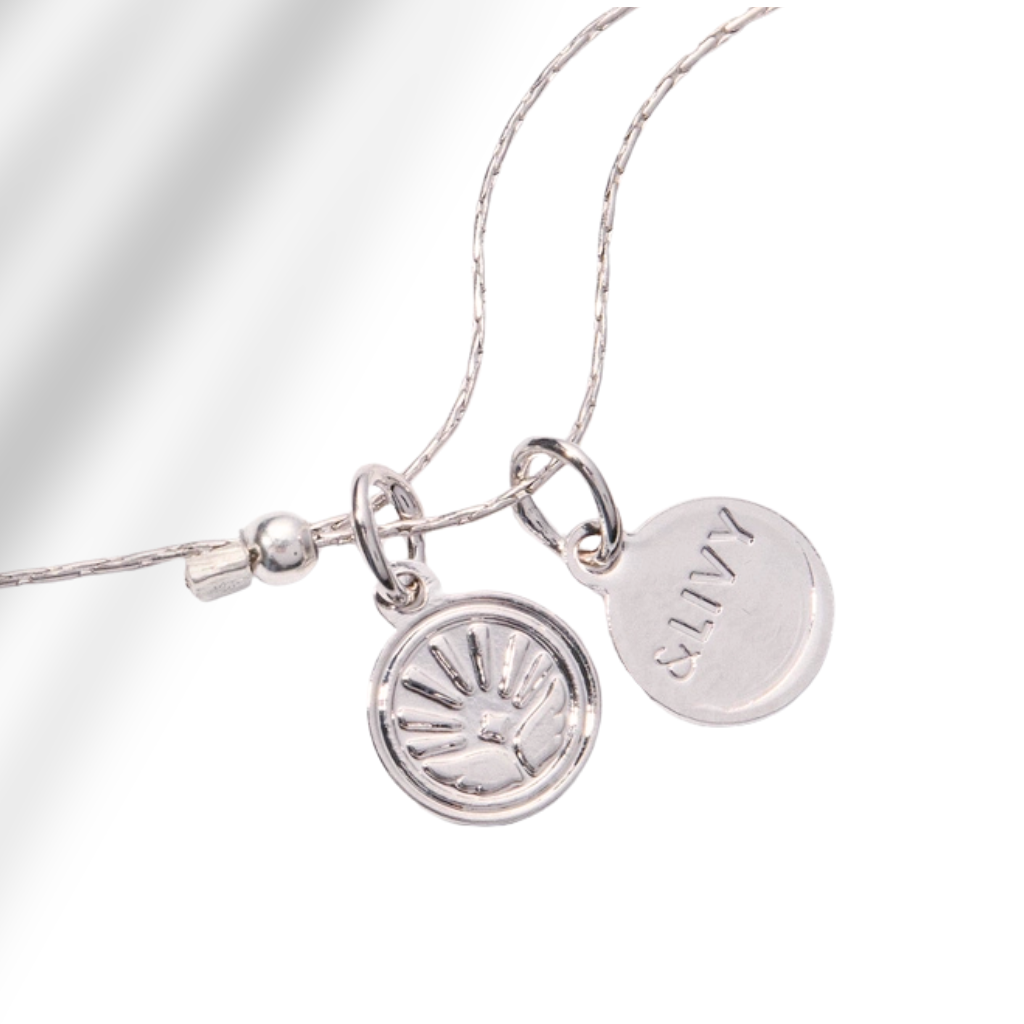 A close-up of a silver necklace with two round disc charms on a white background. One charm features an engraved sunburst pattern, and the other is engraved with the name 'ELIY'.
