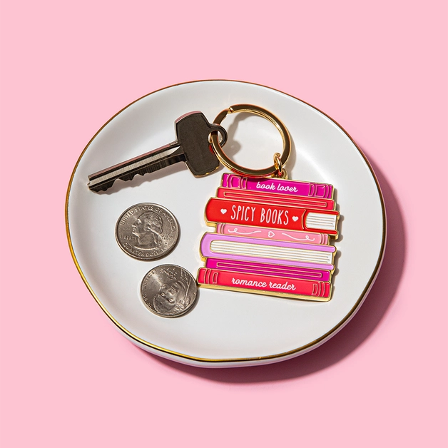 Keychain with book design on a white dish with coins and keys against a pink background