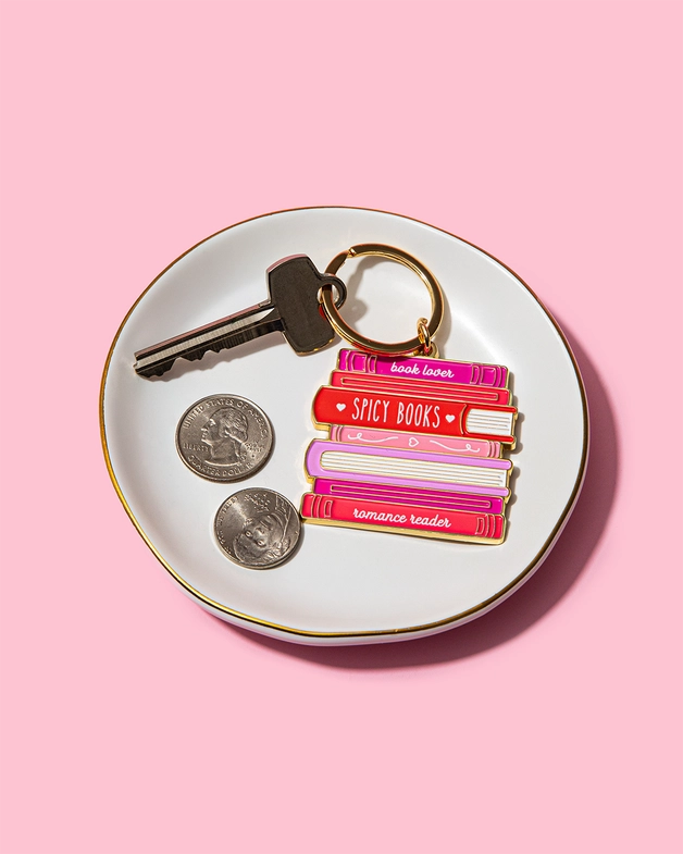 Keychain with book design on a white dish with coins and keys against a pink background