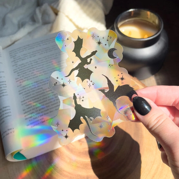 a hand holds a clear window sticker with dragon silhouettes
