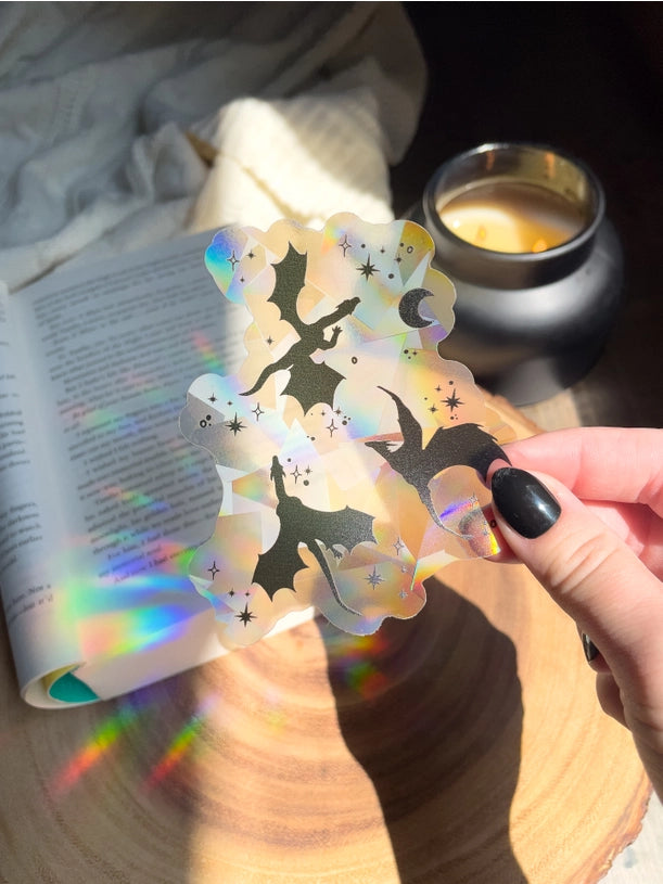 a hand holds a clear window sticker with dragon silhouettes
